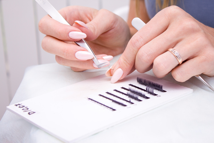 Eyelash Extension Procedure. Woman hands Closeup with tool for eyelash extension. Master of tweezers is working.